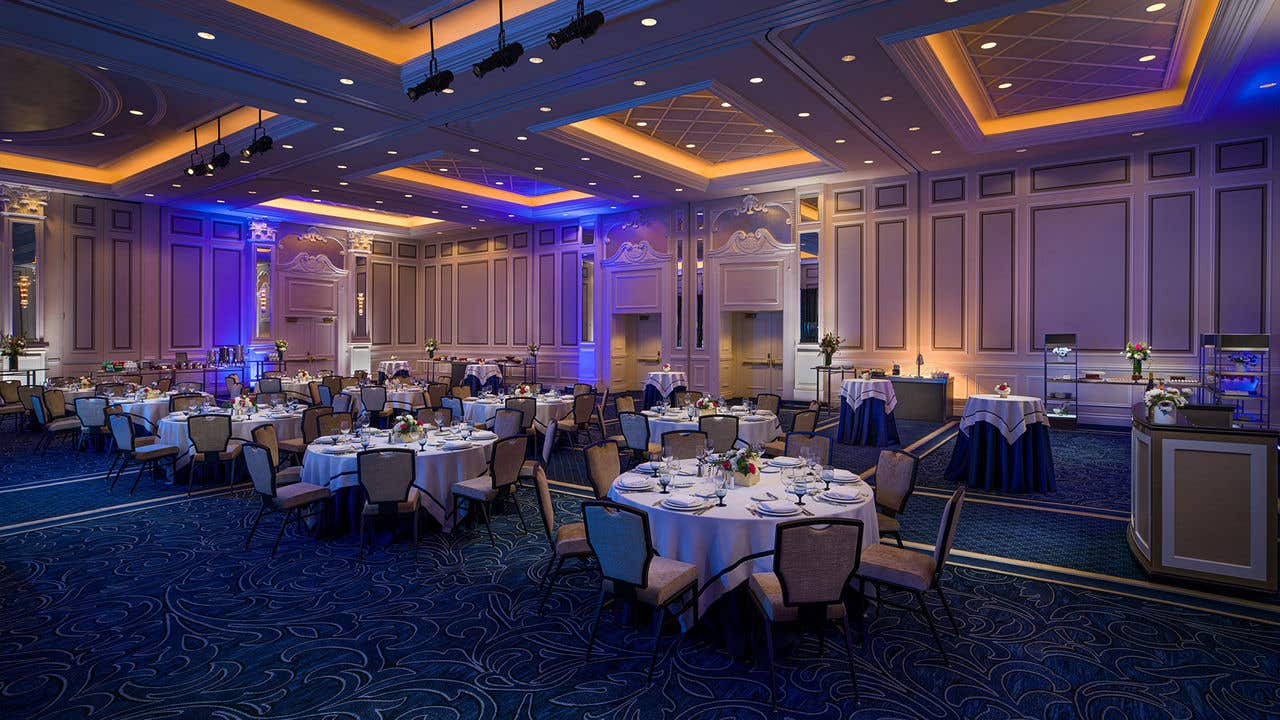 Elegant ballroom set for a banquet, featuring round tables with white linens and navy table accents, complete with place settings and floral centerpieces. 