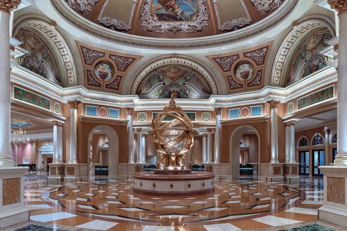 Grand rotunda with ornate columns, painted domed ceiling, and a large golden armillary-style sculpture centered on a patterned marble floor.