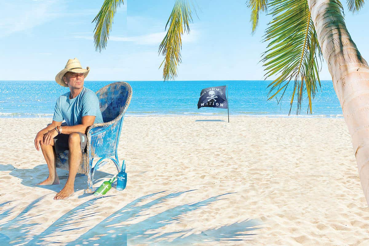 Country singer Kenny Chesney sitting in a blue chair on a beach, wearing a straw cowboy hat.