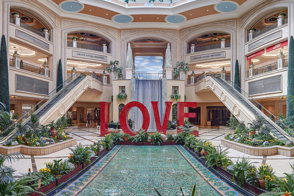 Red structure spelling out the word “LOVE” stands in an atrium, flanked by escalators and a waterfall behind it. 