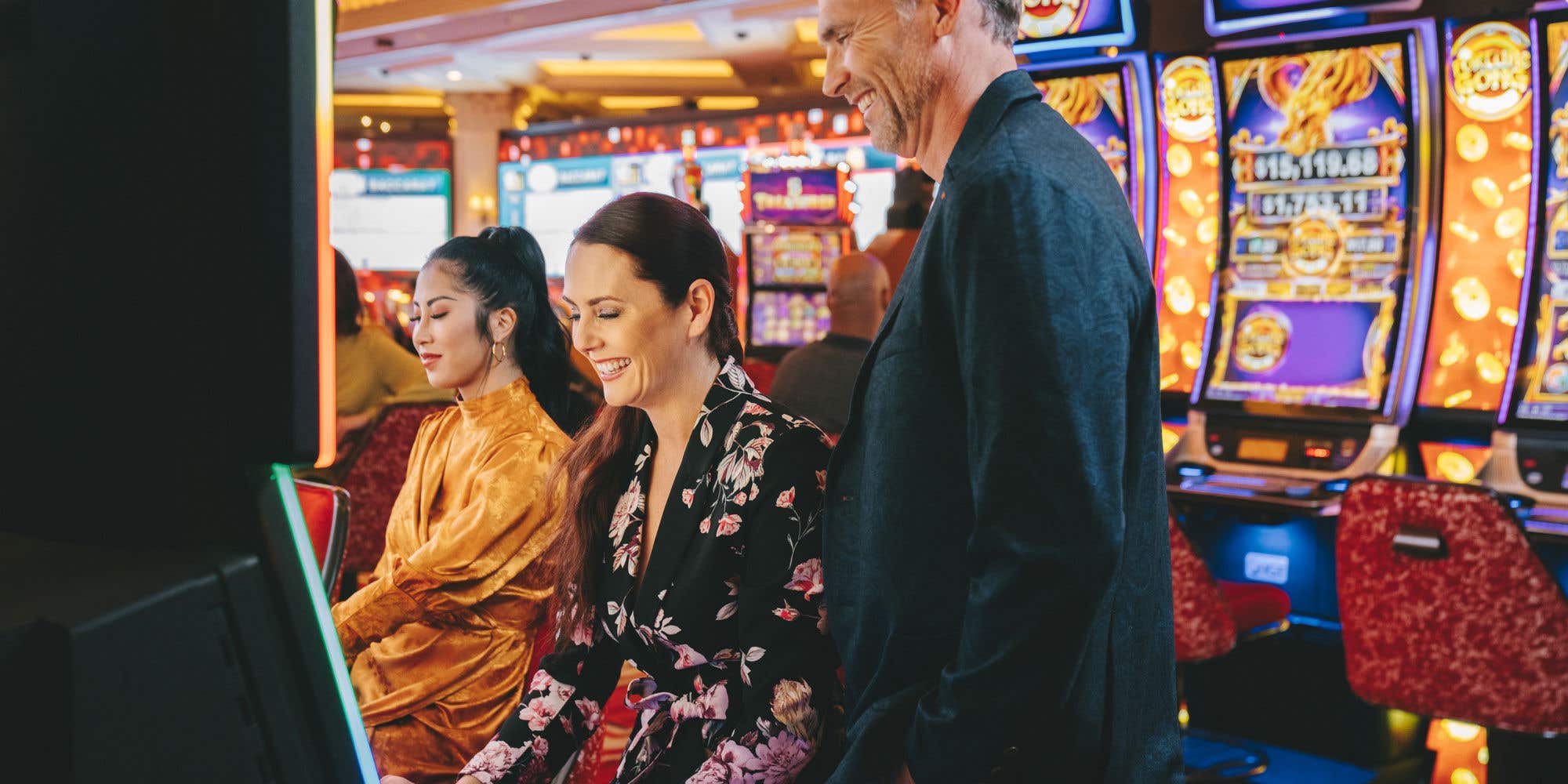 A man and two women gambling and smiling at a slot machine on The Venetian casino floor.