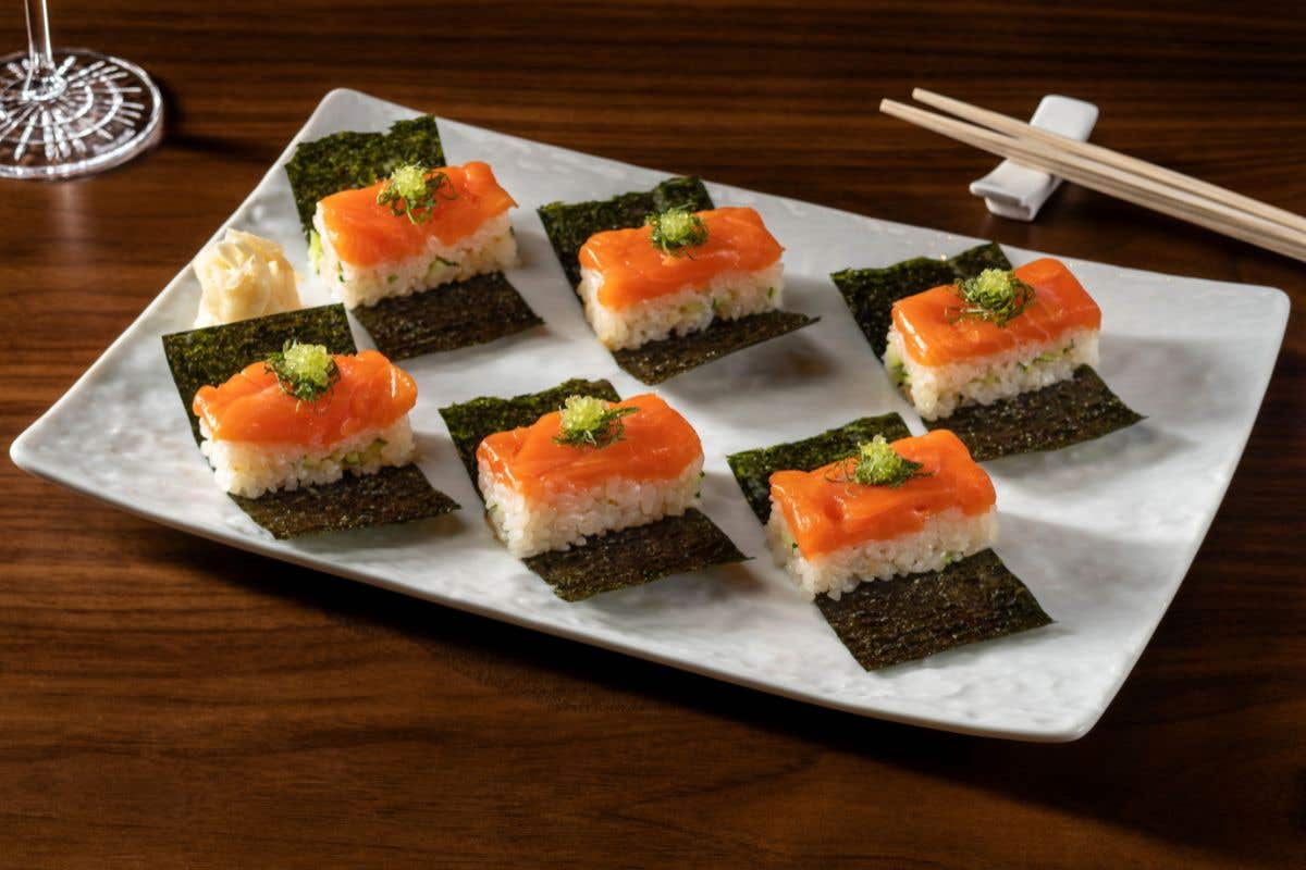 Salmon and rice bites served on seaweed sheets with chopsticks.