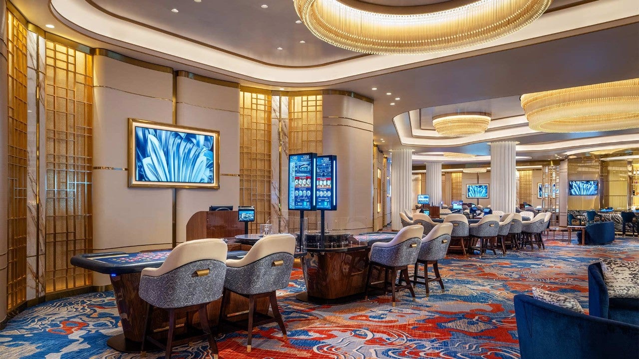 A luxurious casino lounge with gaming tables, seating areas, and video screens.