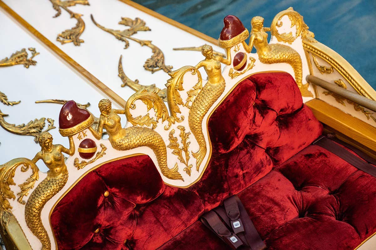 Ornate golden carriage with red velvet interior and intricate mermaid designs on the headrest.
