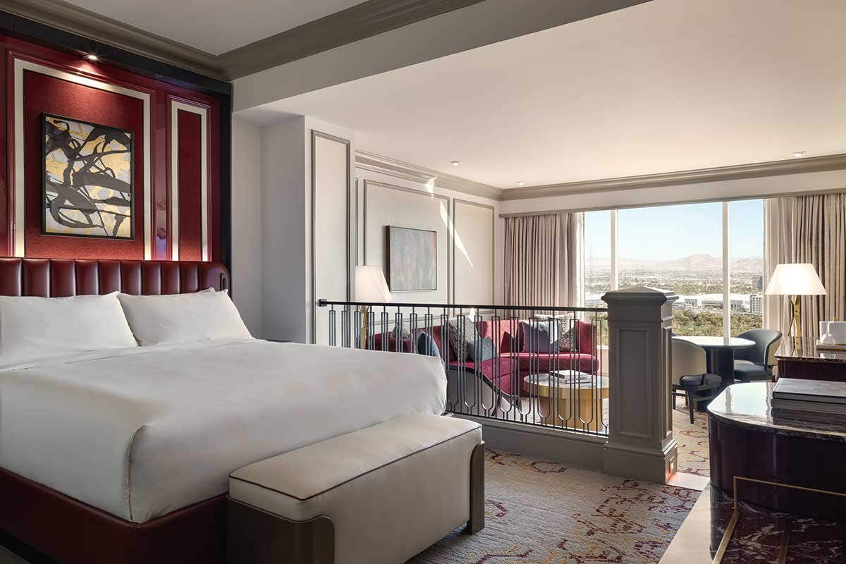 Newly Remodeled Luxury King Suite with a white bed, abstract art, and a living area with a red sofa, framed by a large window showing a city view.