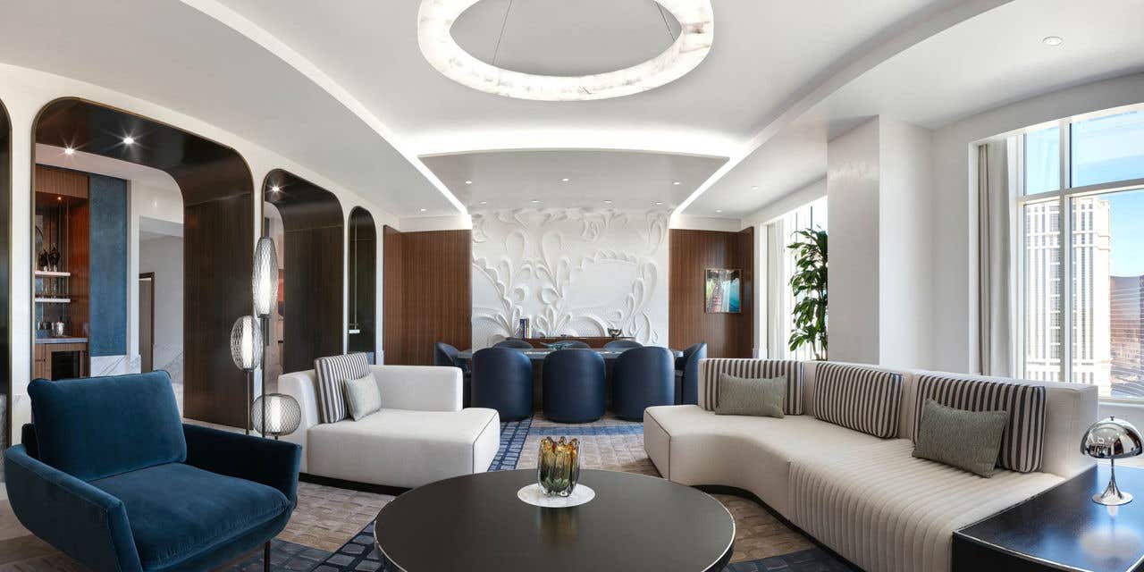 A white and blue hotel living room with a couch, coffee table, chairs, and a dining table with eight chairs.