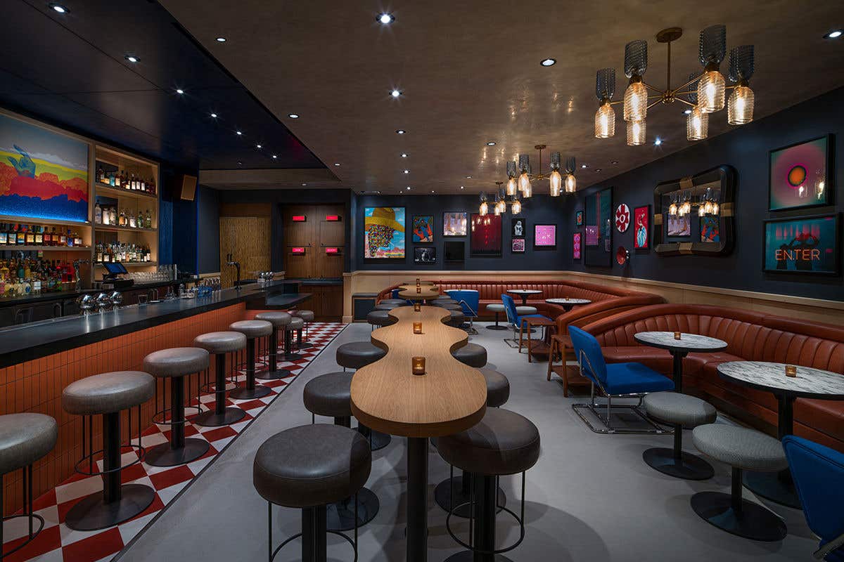 Dim lit bar with colorful artwork on the walls with table, stool and chairs. 