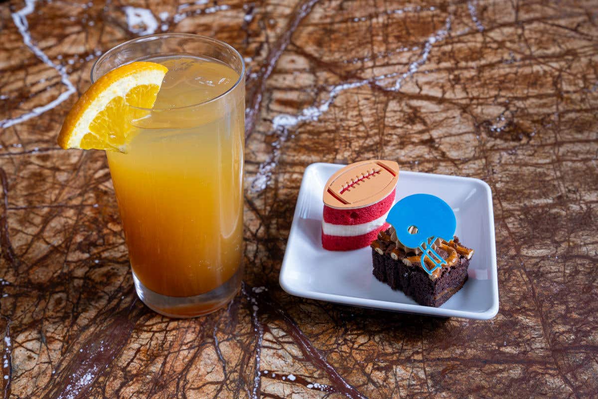 A brown stone surface with a beer cocktail and a small white plate with two football-themed desserts on it.