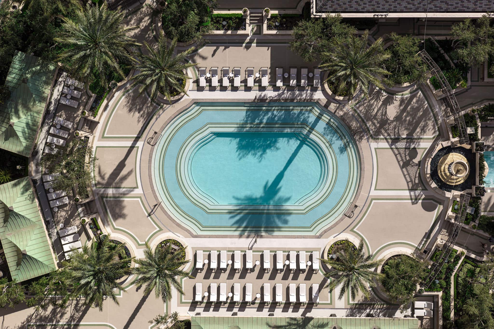 Aerial view of a luxurious pool surrounded by palm trees and lounge chairs, with geometric patterns on the pool deck.