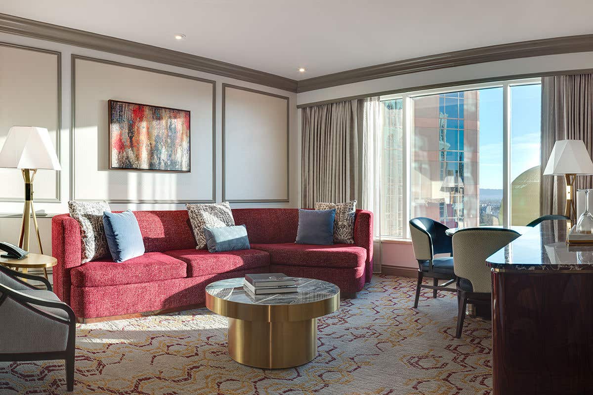 Remodeled Luxury King Suite living room with an armchair, couch, coffee table, dining table with chairs, lamps, and a view of Sphere at The Venetian outside the window.