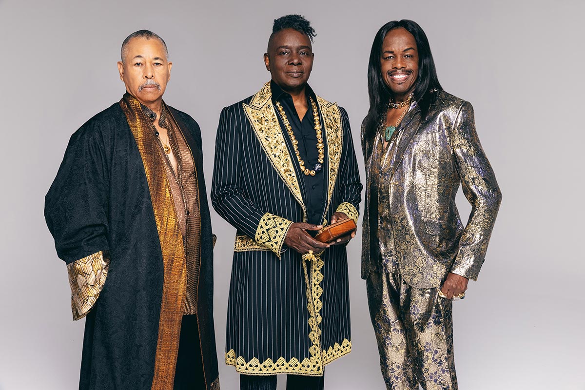 Three men in ornate suits stand side by side, smiling against a plain background, showcasing their detailed attire.
