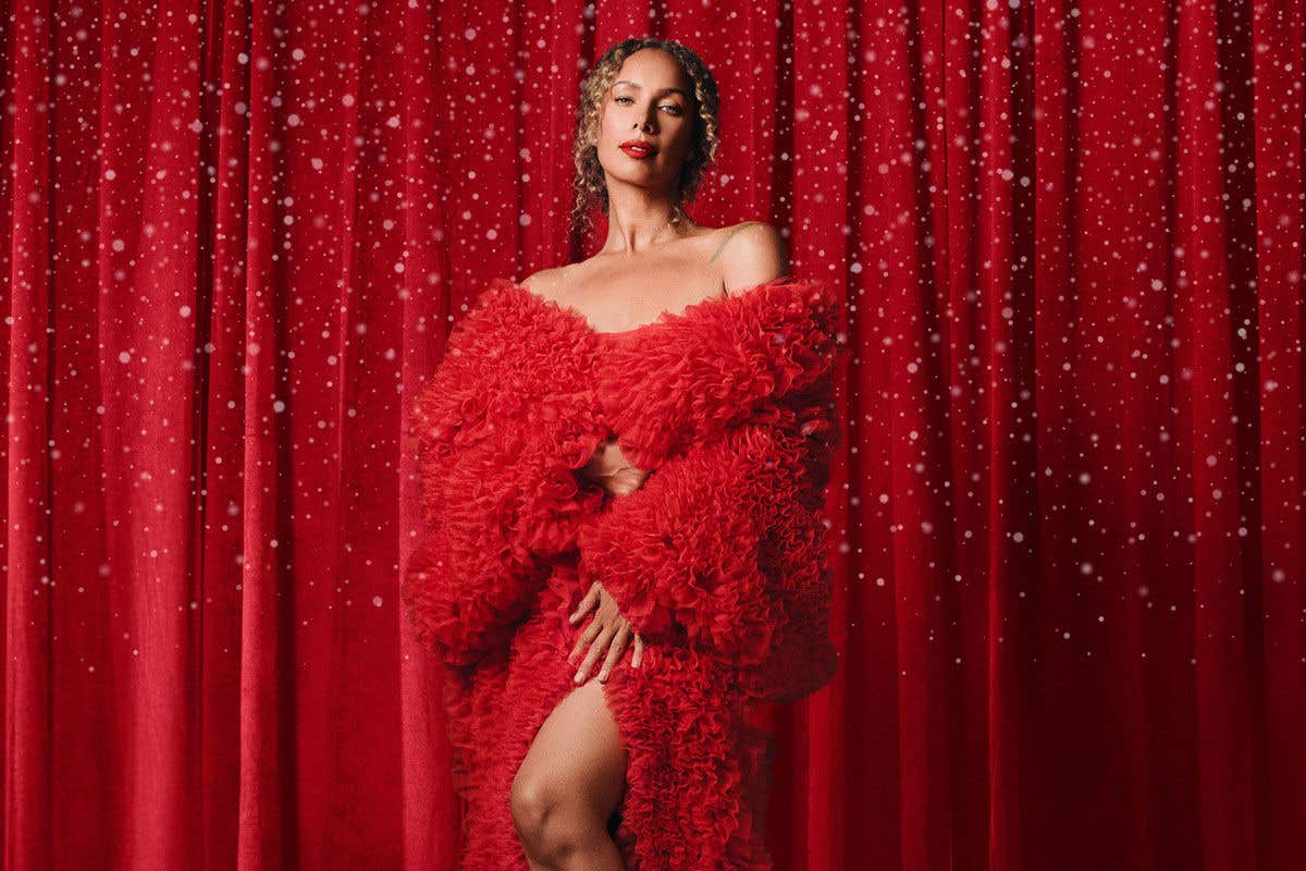 Leona Lewis in red dress in front of red curtain background with snow falling all around her. 