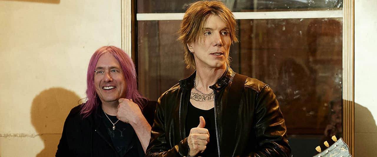 Goo Goo Dolls the band standing in front of a building holding guitars and looking off to the distance.  