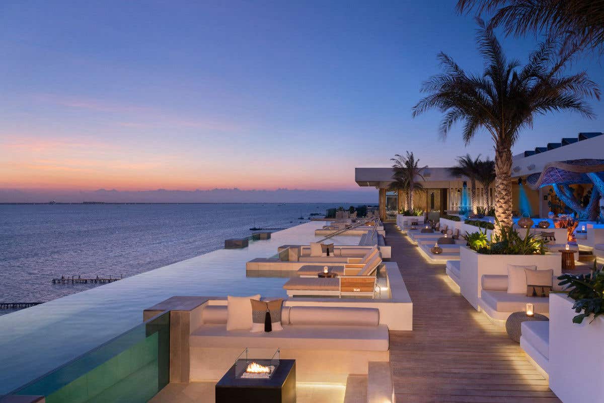 Luxury oceanfront terrace with lounge seating, palm trees, and an infinity pool at sunset.