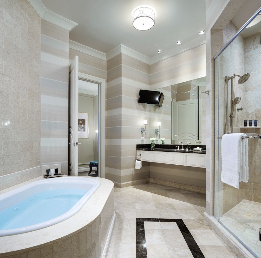 Modern bathroom with a soaking tub, glass-enclosed shower, and vanity under a wall-mounted TV, all in a neutral palette.