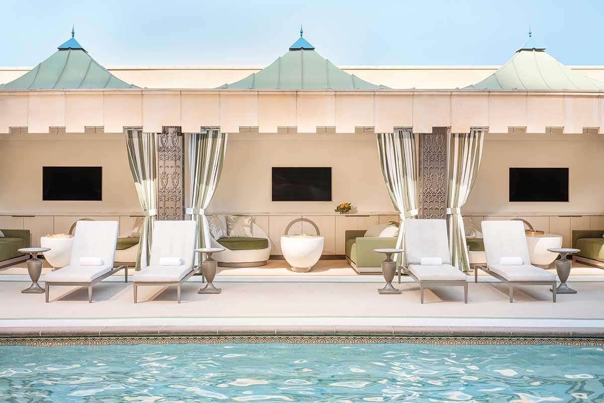 Three standard Palazzo cabanas poolside, each with a TV, couch, coffee table, armchair, and lounge chairs in front. 