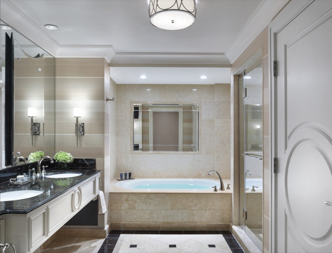 Elegant bathroom with a bathtub, double sinks, large mirror, and a glass-enclosed shower under soft ceiling lights.
