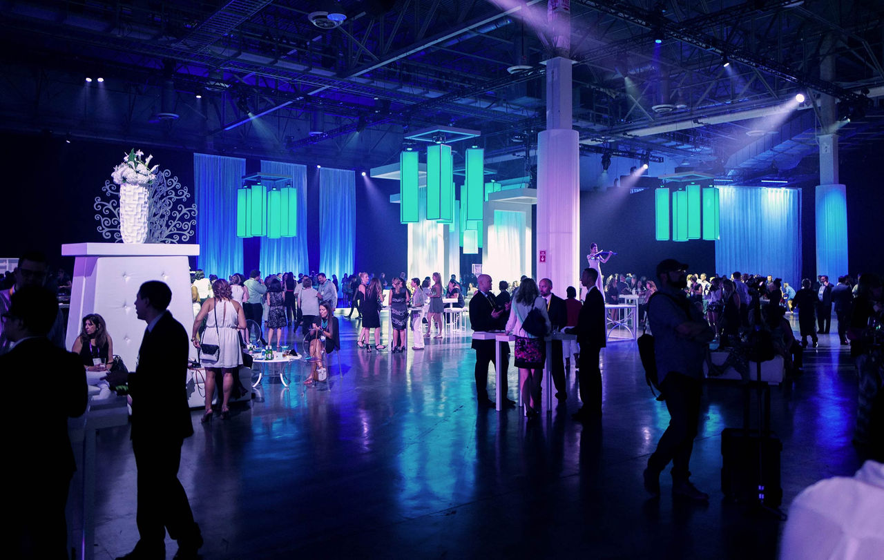 A dark lit expo hall with people mingling during an event. 